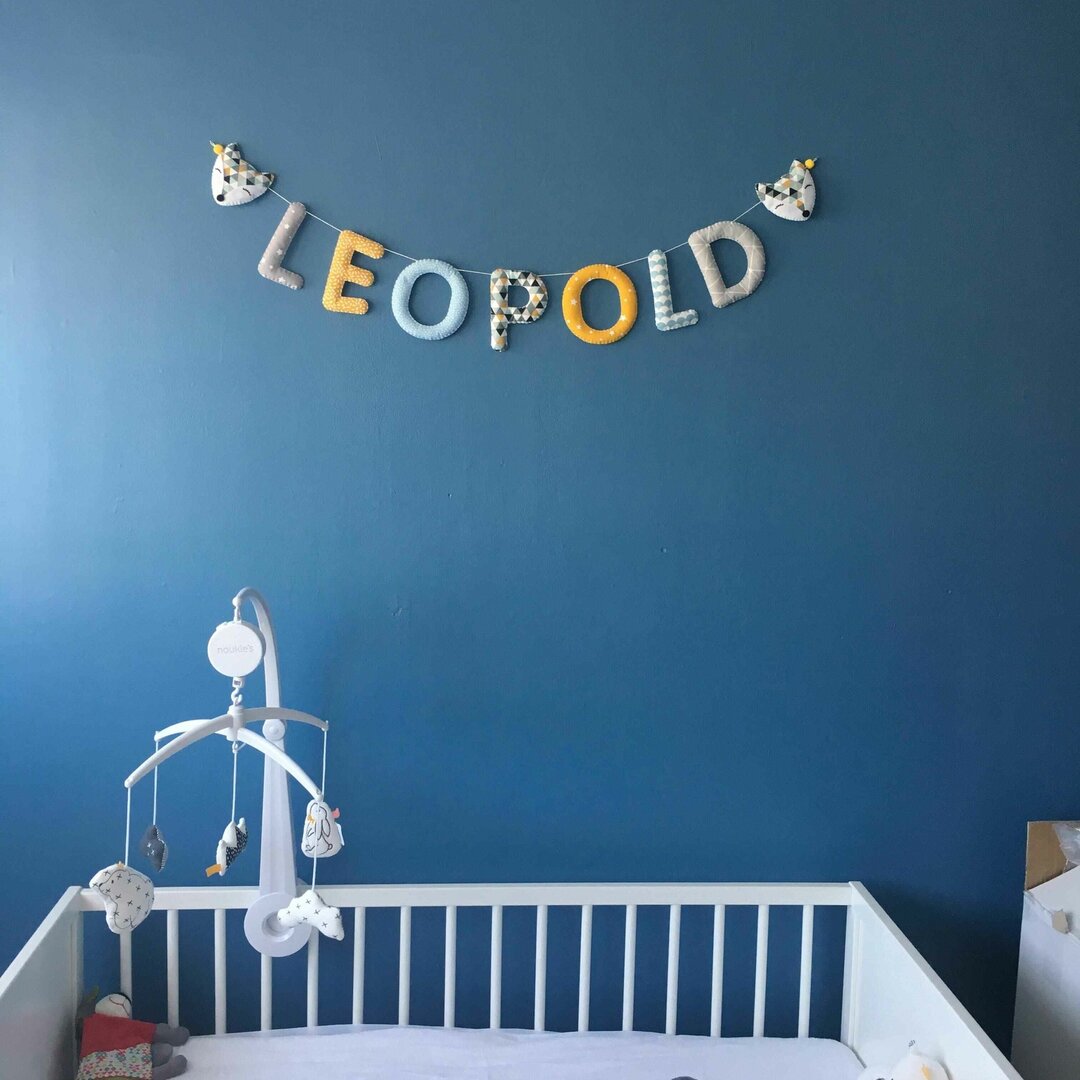 Guirlande prénom en tissu bleu et jaune moutarde avec embouts renard, exemple « Léopold », au-dessus d'un lit à barreaux