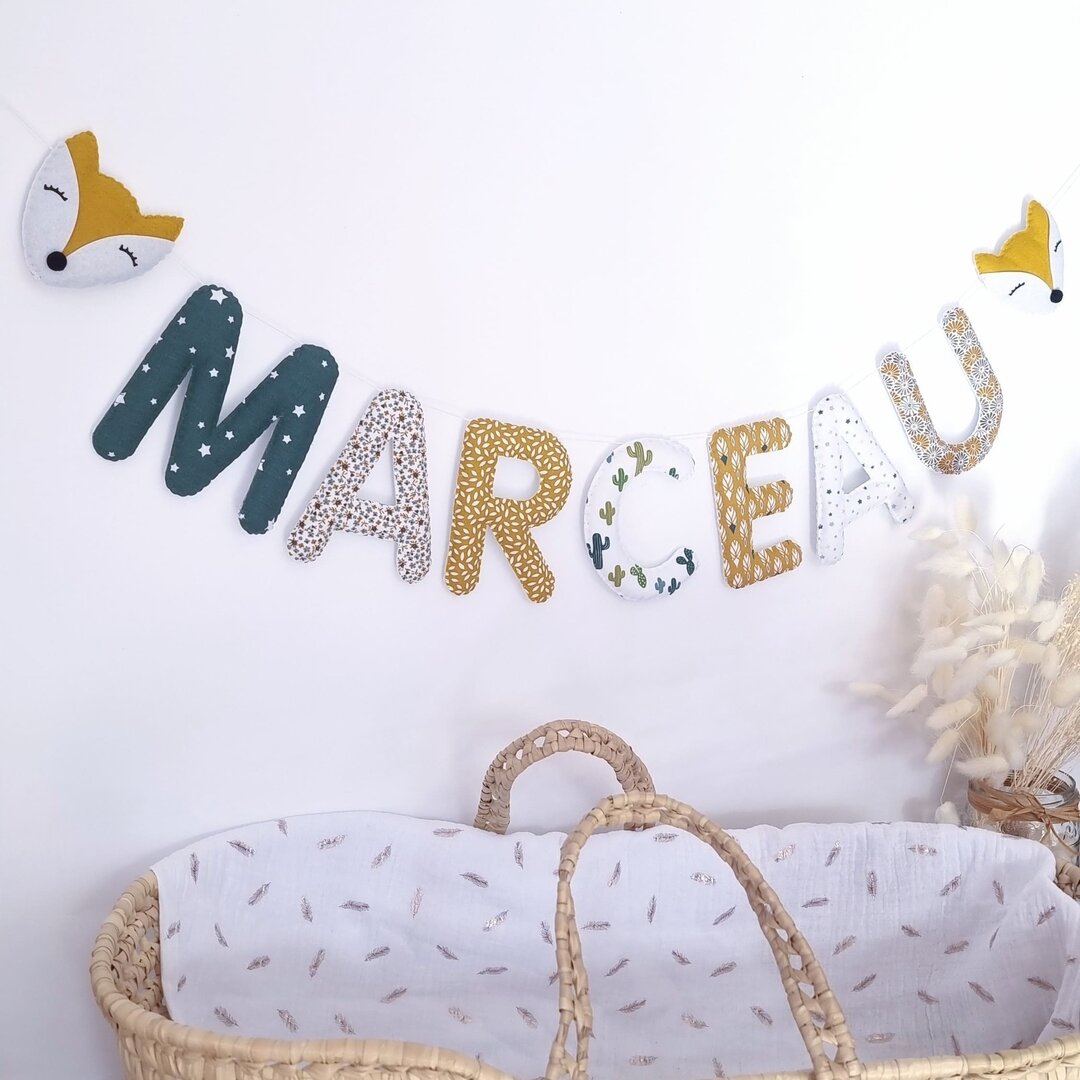 Exemple de guirlande prénom personnalisée dans des tissus vert et jaune moutarde, avec têtes de renard, au-dessus d'un couffin