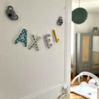 Guirlande prénom bleu canard et gris posée sur une porte de chambre bébé garçon