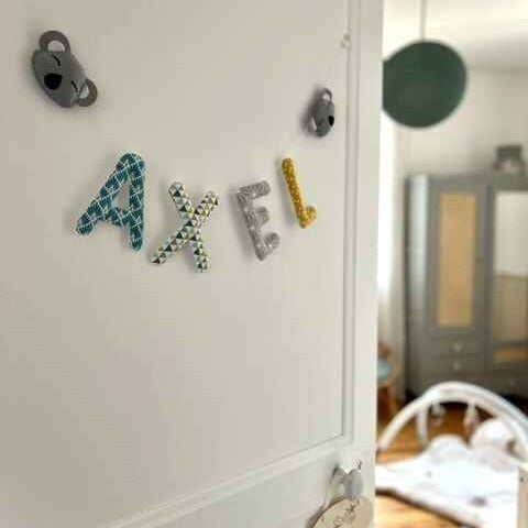Guirlande prénom bleu canard et gris posée sur une porte de chambre bébé garçon